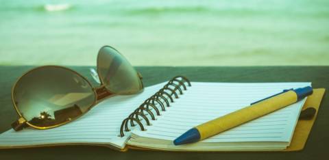 glasses, notebook and pen with ocean behind